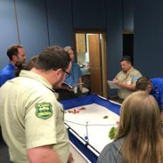 Group of students standing around an activity box, listening to instructor