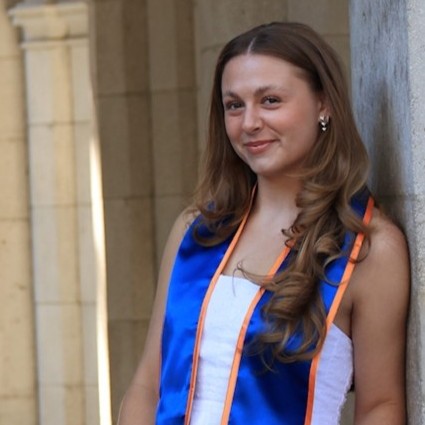 Hannah leaning against a wall, wearing college graduation attire