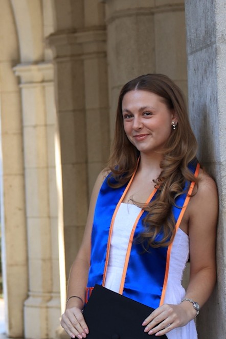 Hannah leaning against a wall, wearing college graduation attire