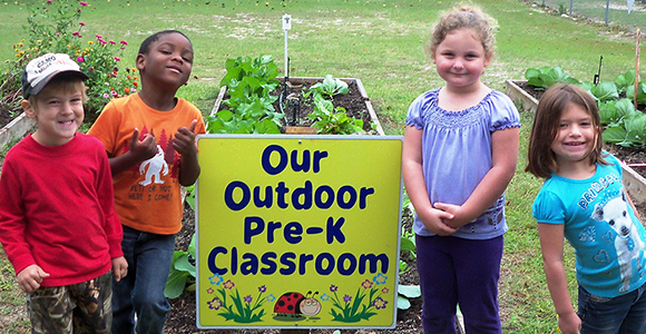 Preschool students standing around a sign saying 